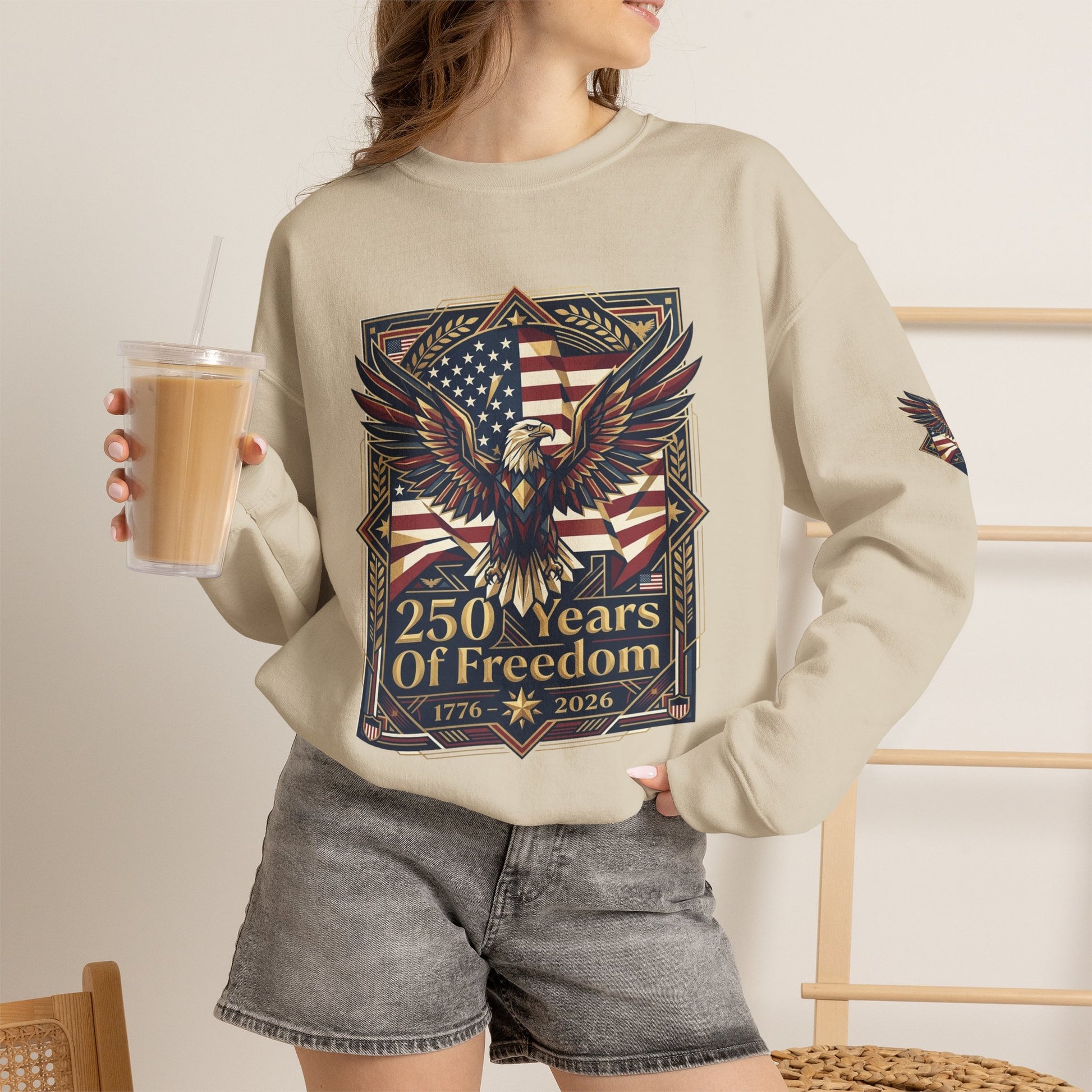 USA 250th ANNIVERSARY Crewneck Sweatshirt , Person wearing a beige sweatshirt with an eagle and American flag design, holding a drink.