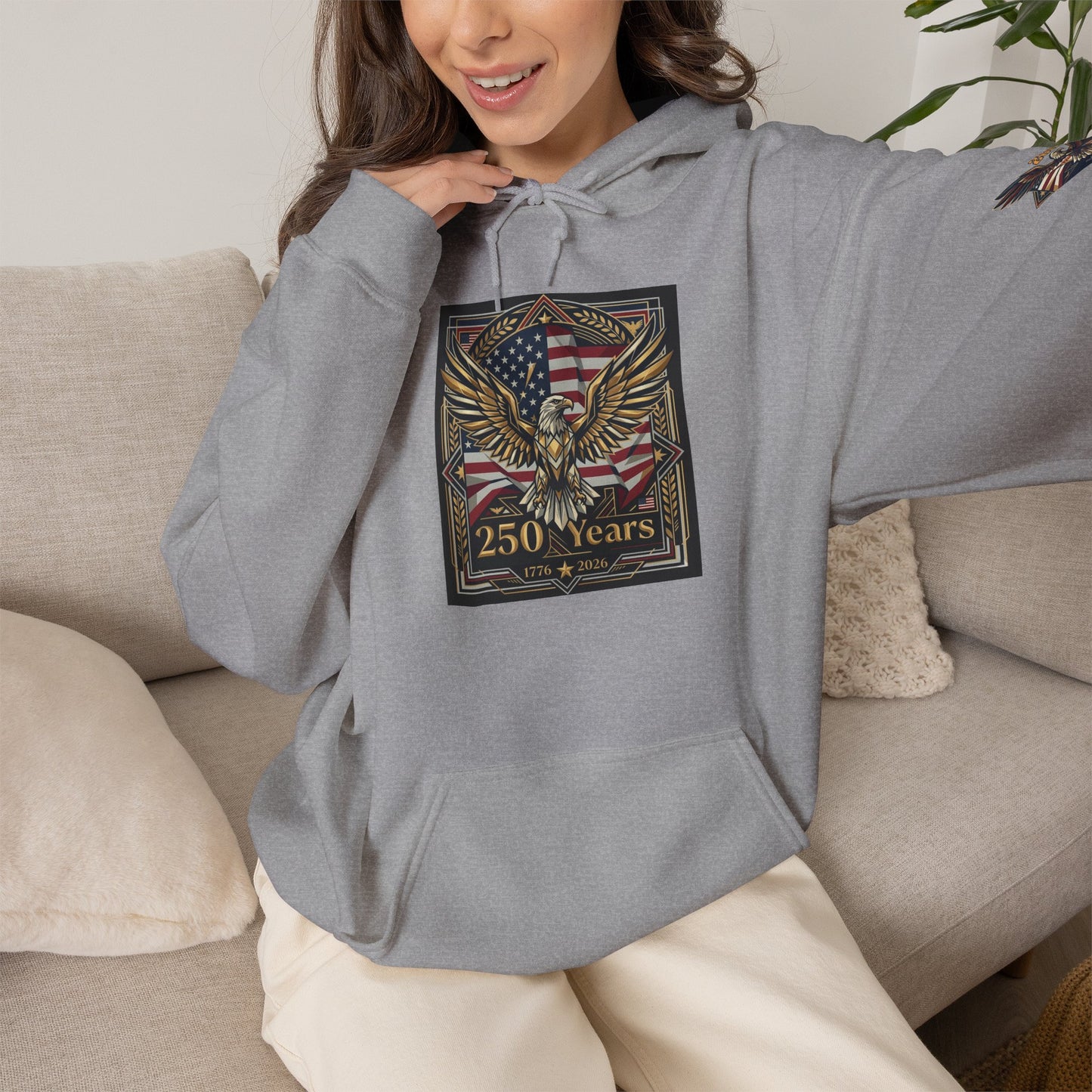 America 250 Years of Freedom Hoodie — USA 250th ANNIVERSARY Patriotic Hoodie, Person wearing a gray hoodie with an eagle and flag design, sitting on a couch.
