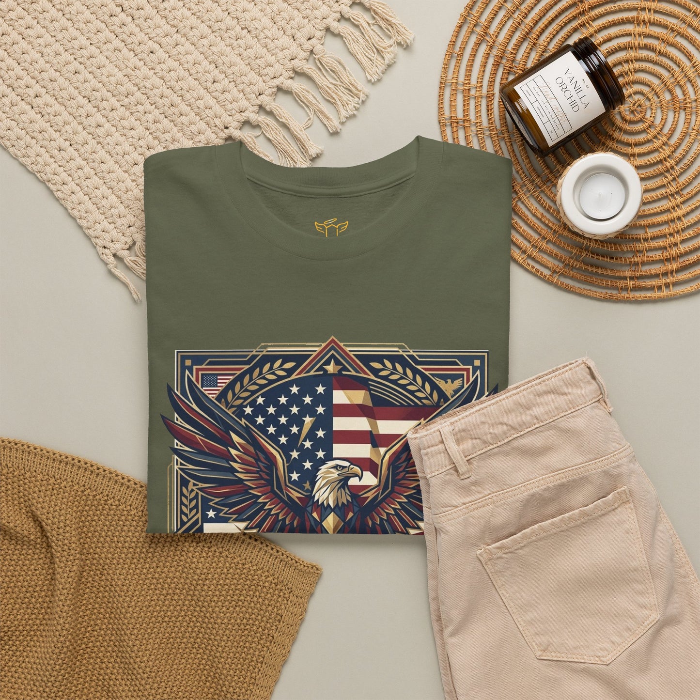 Green t-shirt with eagle and American flag design on a neutral surface with pants and decor items.