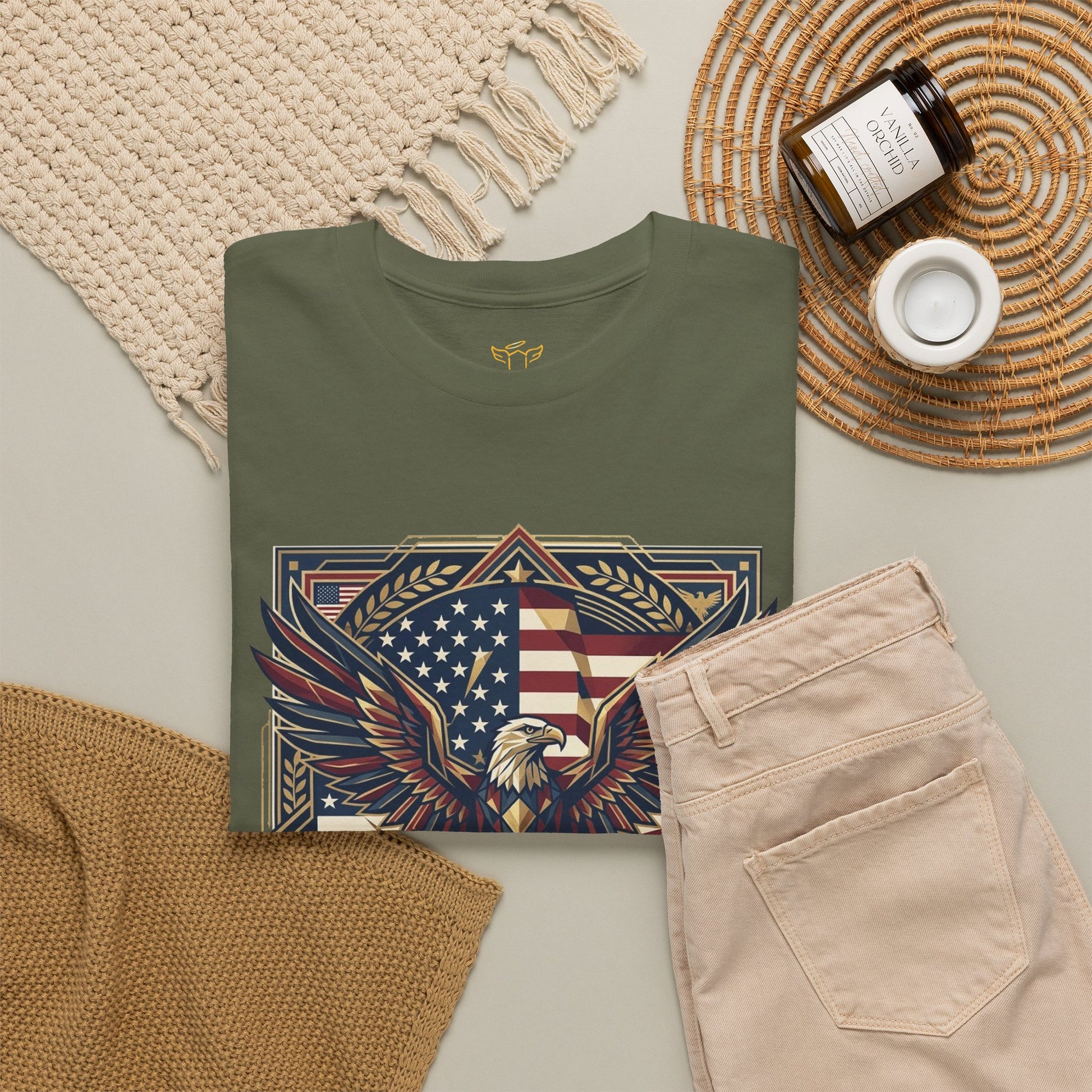 Green t-shirt with eagle and American flag design on a neutral surface with pants and decor items.