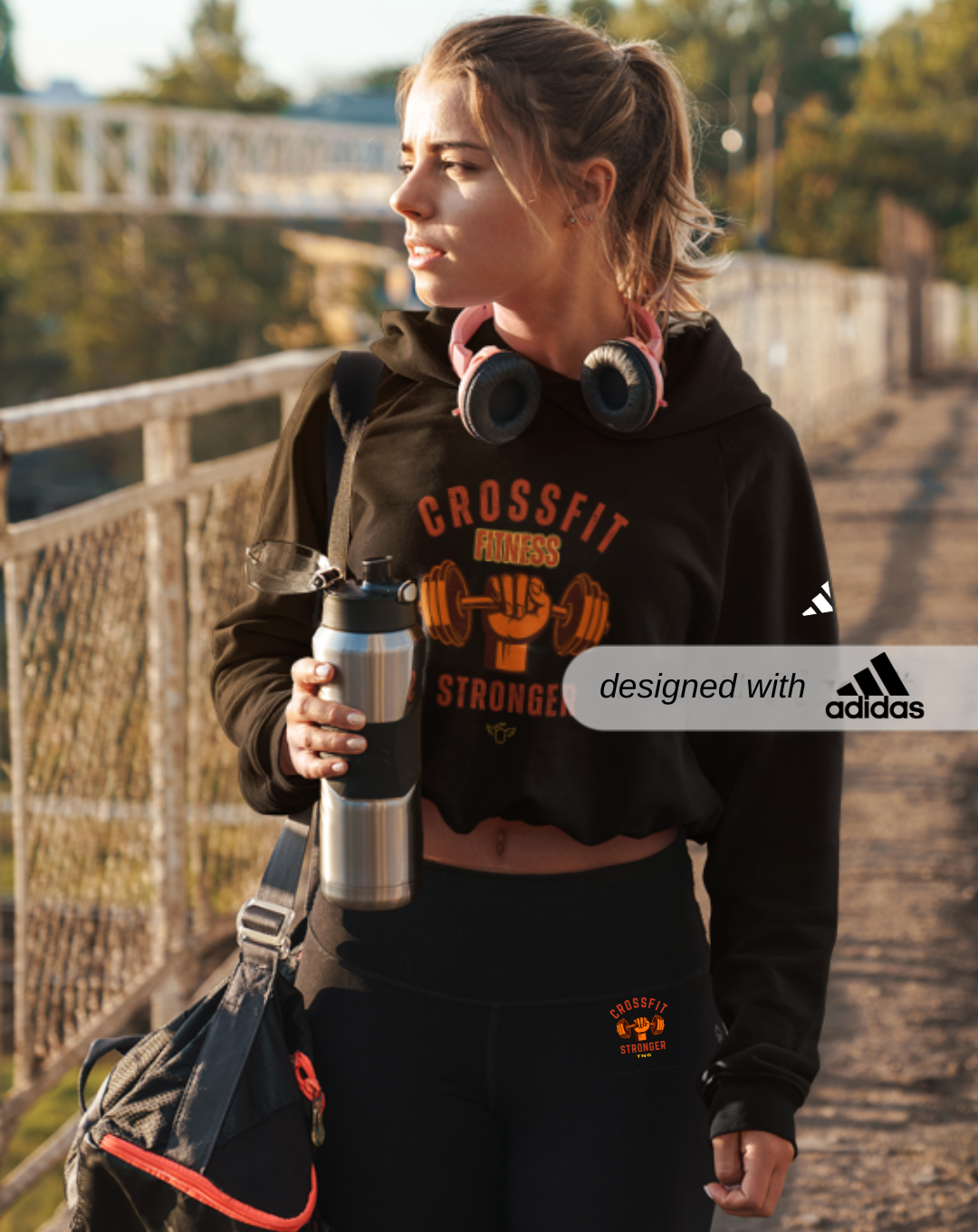 Adidas Sports Hoodie for CrossFit Fans, Adidas CrossFit Hoodies, Woman in a CrossFit-themed hoodie holding a water bottle on a bridge