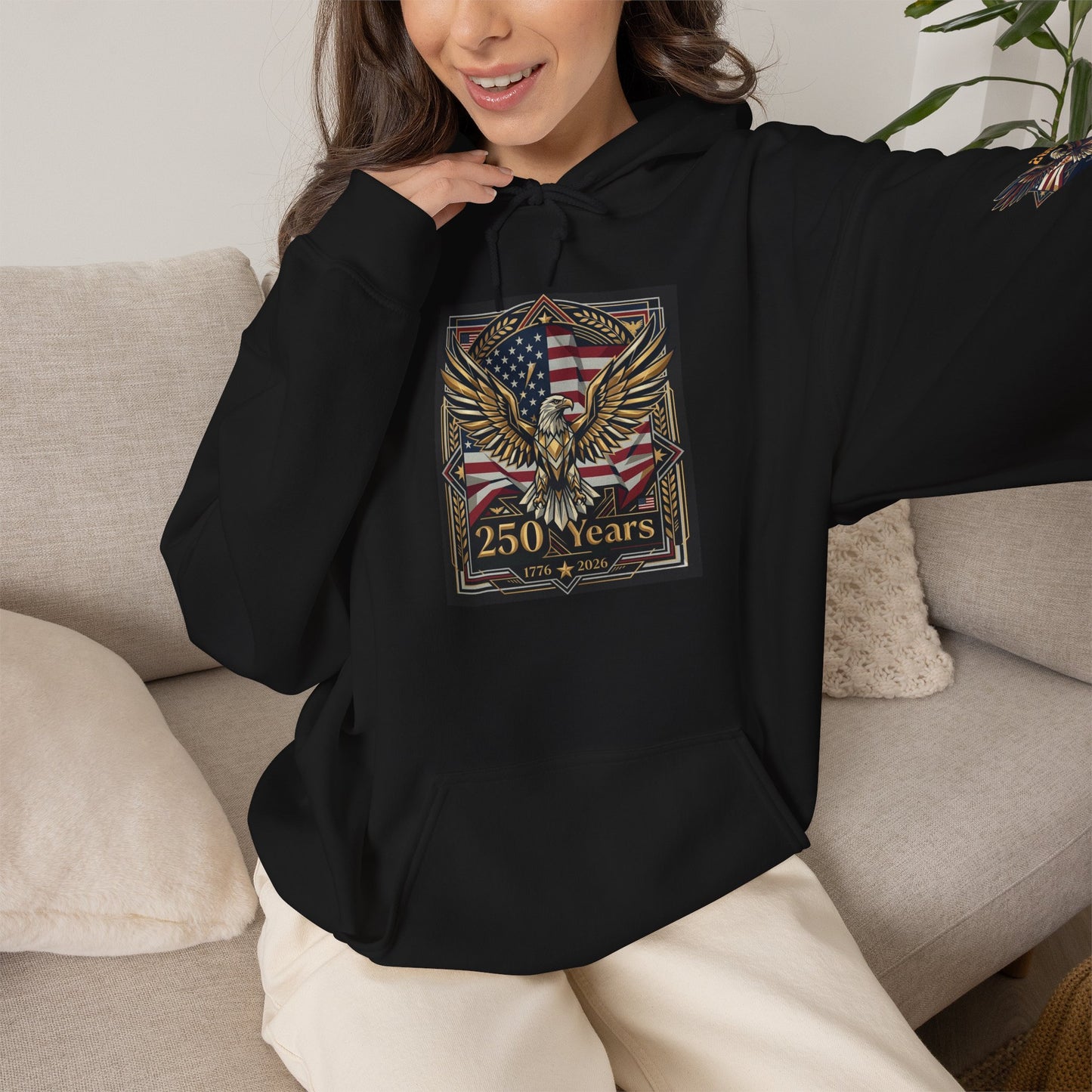 America 250 Years of Freedom Hoodie — USA 250th ANNIVERSARY Patriotic Hoodie, Person wearing a black hoodie with an eagle and American flag design, sitting on a couch.