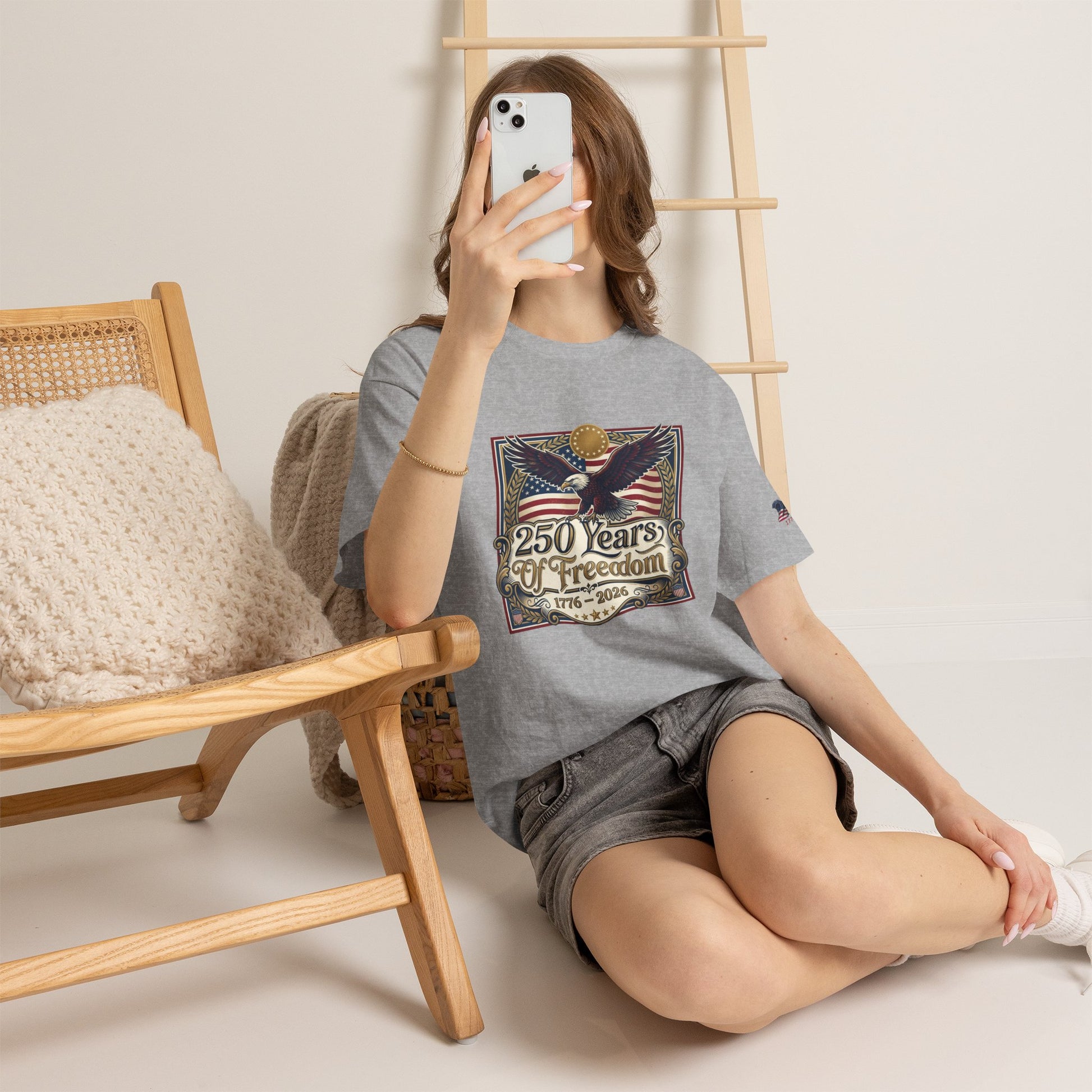 250 Years of Freedom T-Shirt — USA 250TH Anniversary Patriotic Eagle Tee, Person wearing a gray t-shirt with a graphic design, sitting on the floor with a wooden chair and ladder in the background.
