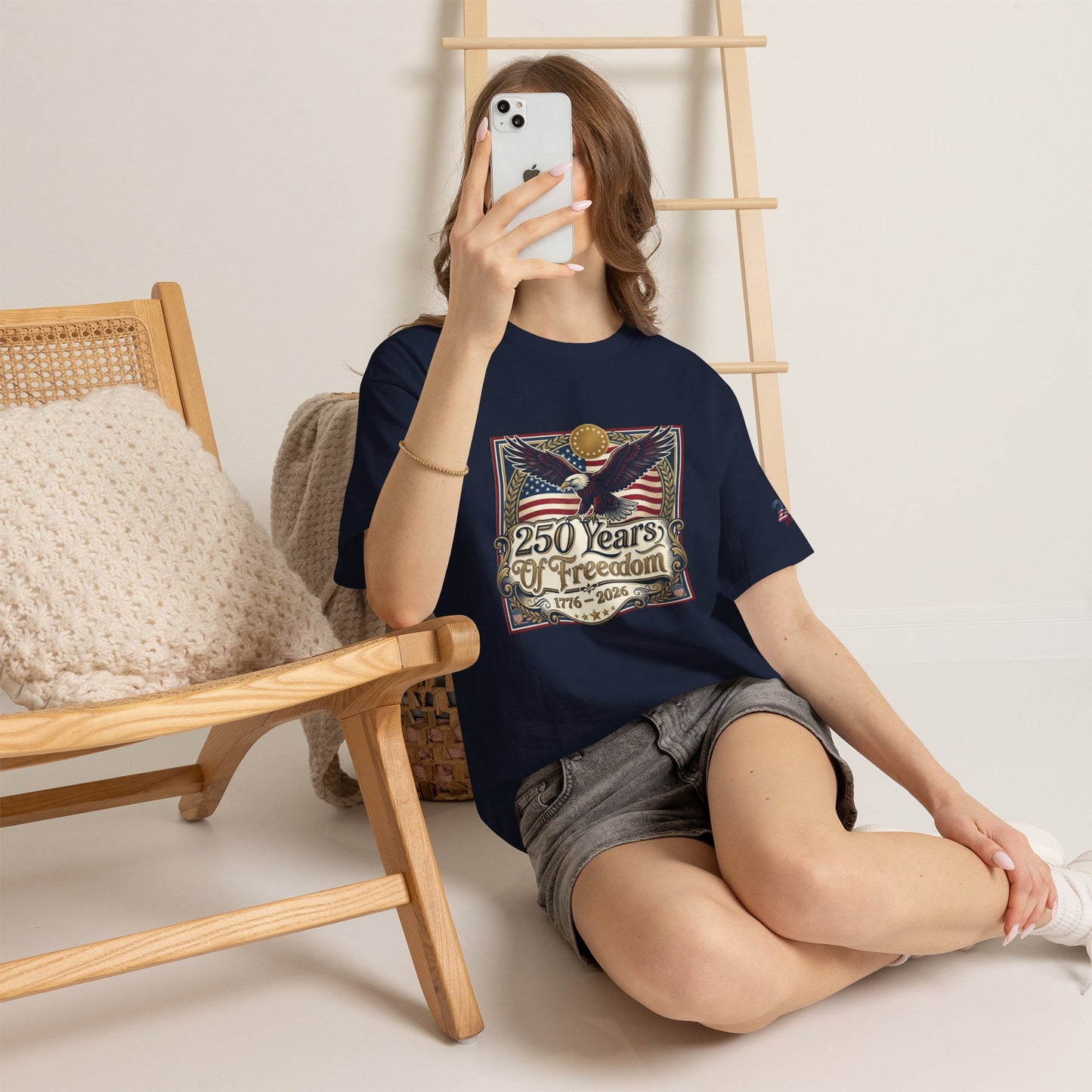 250 Years of Freedom T-Shirt — USA 250TH Anniversary Patriotic Eagle Tee, Person wearing a black t-shirt with a graphic design, sitting on the floor with a wooden chair and ladder in the background.