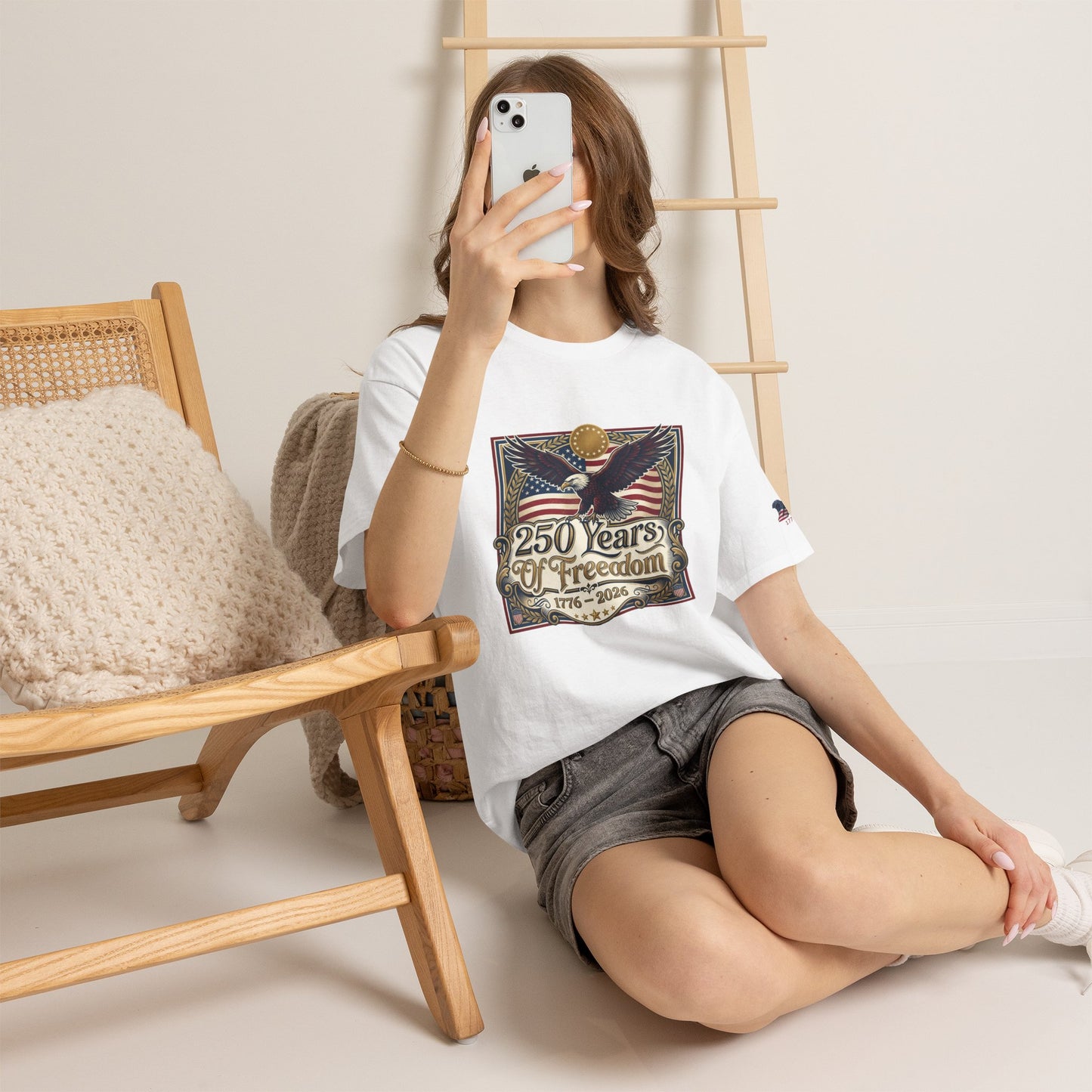 250 Years of Freedom T-Shirt — USA 250TH Anniversary Patriotic Eagle Tee, Person sitting on the floor holding a phone, wearing a white t-shirt with a graphic design.