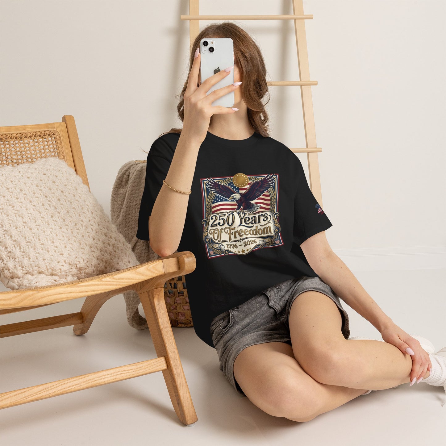 250 Years of Freedom T-Shirt — USA 250TH Anniversary Patriotic Eagle Tee, Person wearing a black t-shirt with a graphic design, sitting on the floor in a room with wooden furniture.