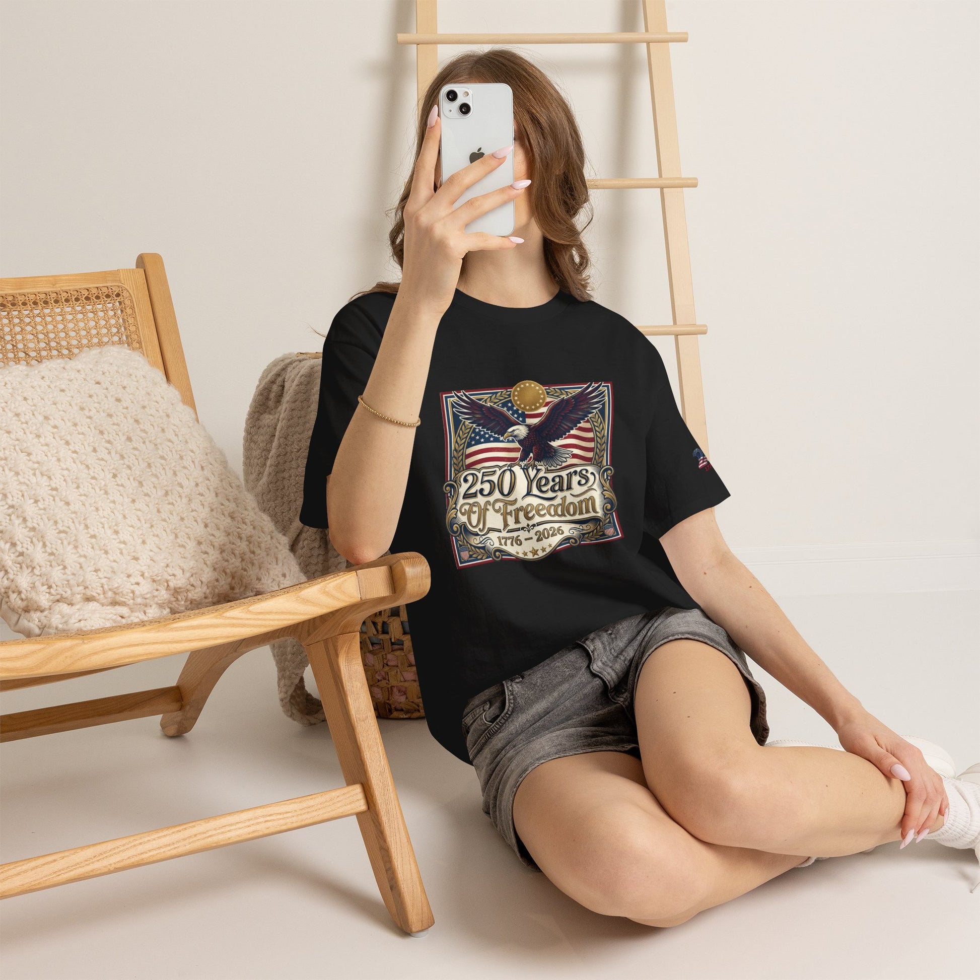 250 Years of Freedom T-Shirt — USA 250TH Anniversary Patriotic Eagle Tee, Person wearing a black t-shirt with a graphic design, sitting on the floor in a room with wooden furniture.