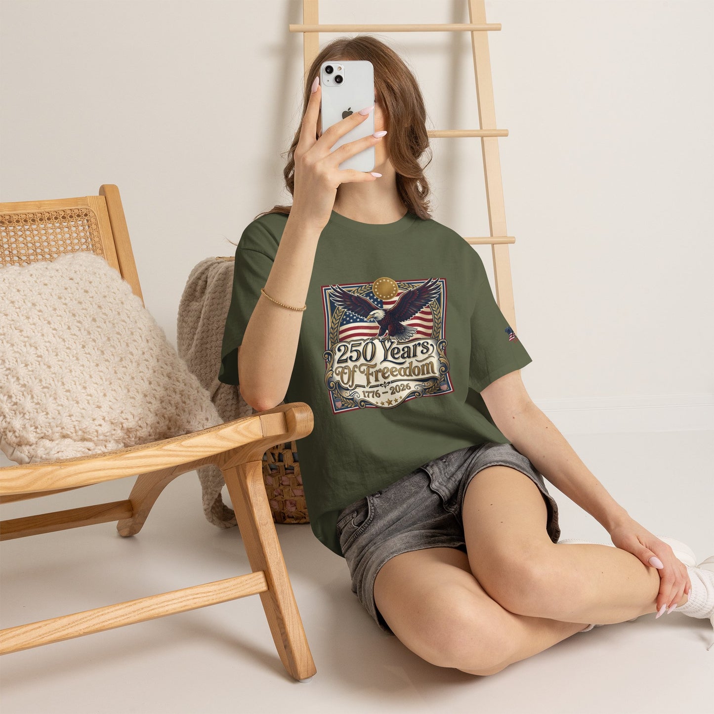 250 Years of Freedom T-Shirt — USA 250TH Anniversary Patriotic Eagle Tee, Person wearing a green t-shirt with a graphic design, sitting on the floor with a wooden chair and ladder in the background.