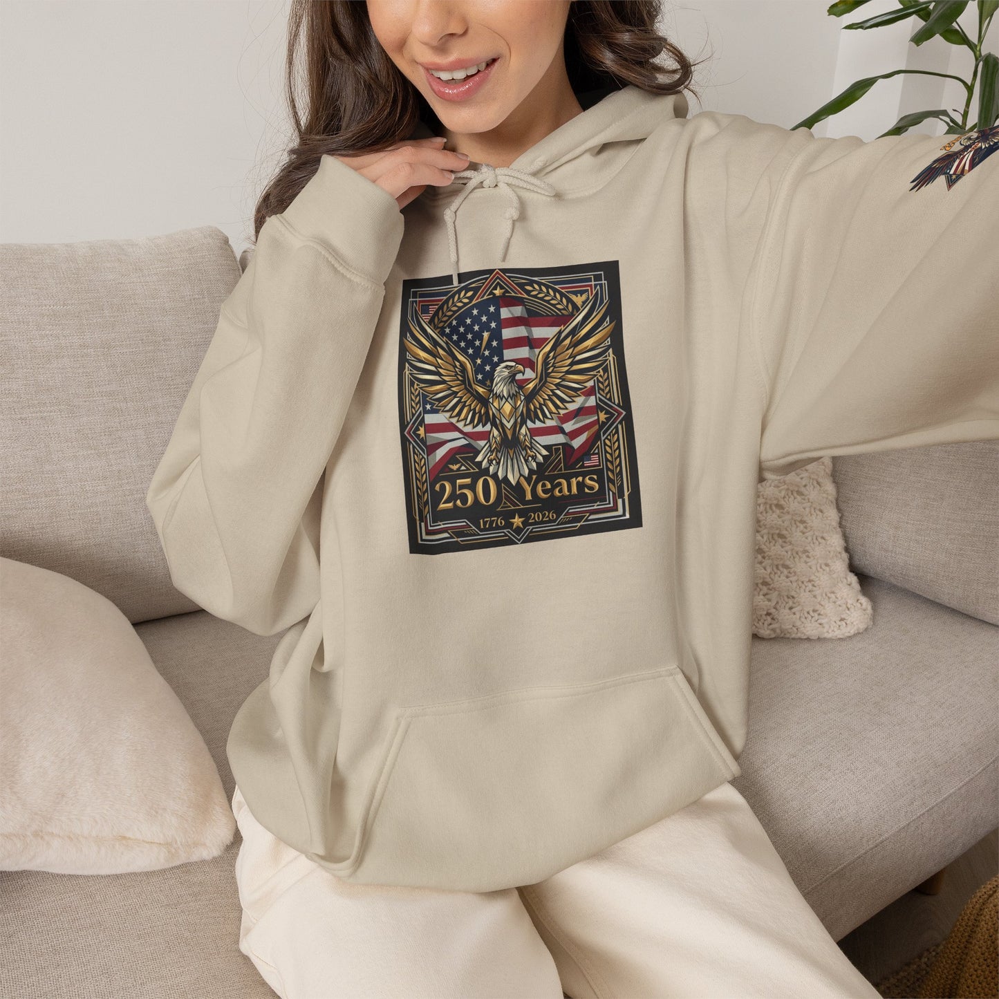 America 250 Years of Freedom Hoodie — USA 250th ANNIVERSARY Patriotic Hoodie, Person wearing a beige hoodie with an eagle and flag design, sitting on a couch.