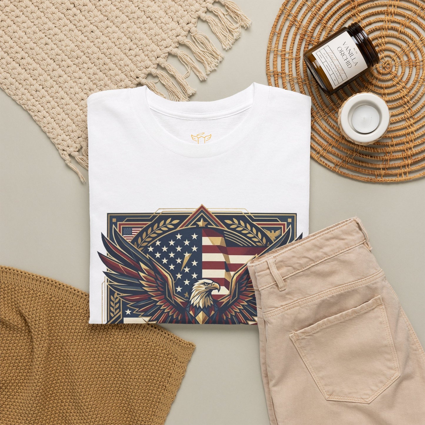 White t-shirt with eagle and American flag design, beige pants, and decorative items on a neutral background